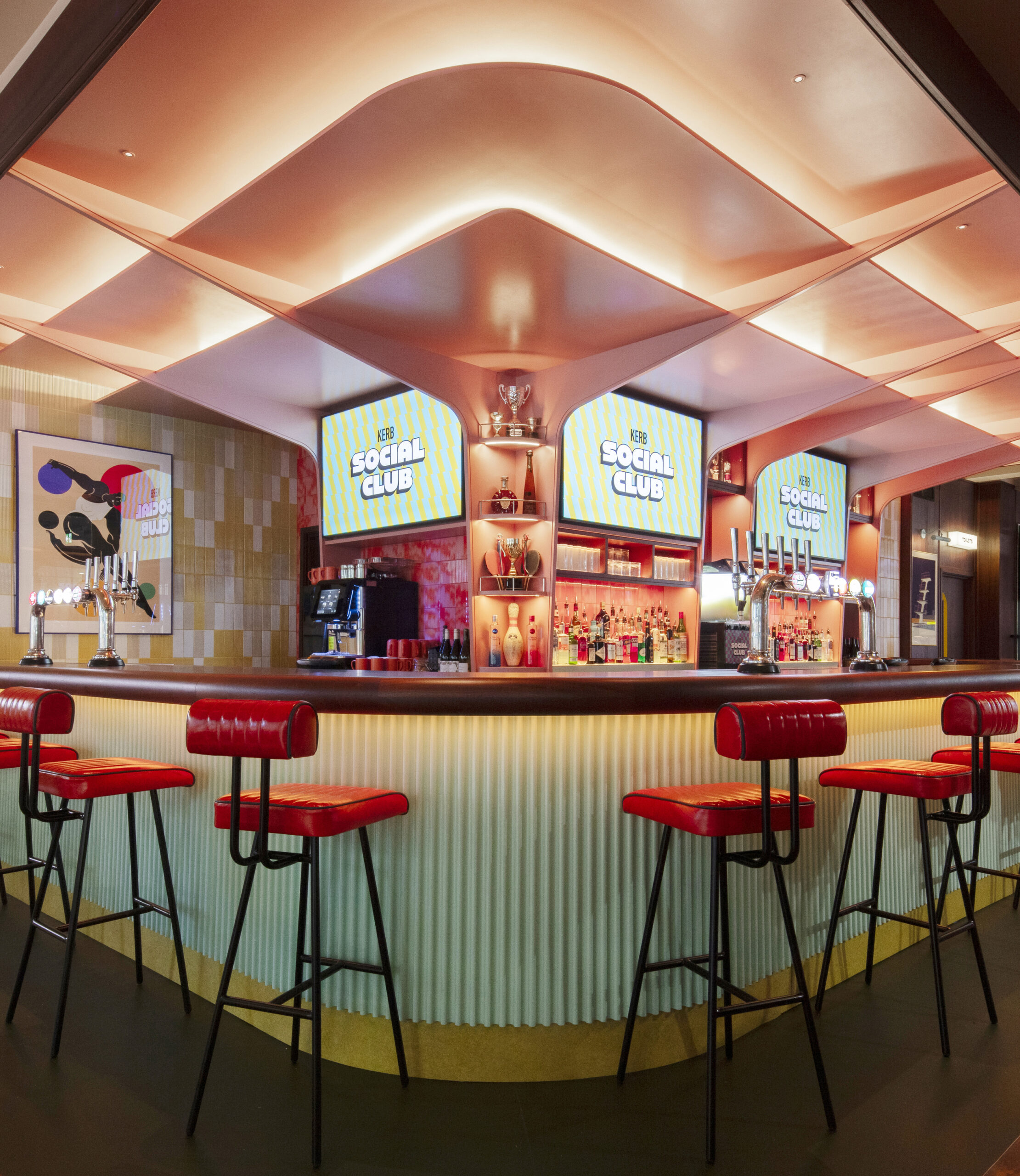 A stylish retro bar with red stools, a curved counter, colourful lighting, and two screens displaying The Social Club above shelves of bottles and glassware. Book KERB Social Club to enjoy modern art walls and illuminated accents.